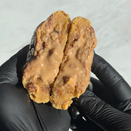 Cookie artisanal XXL coupé en deux avec cœur fondant de nocciolata bianca, éclats de noisettes grillées et chocolat au lait.